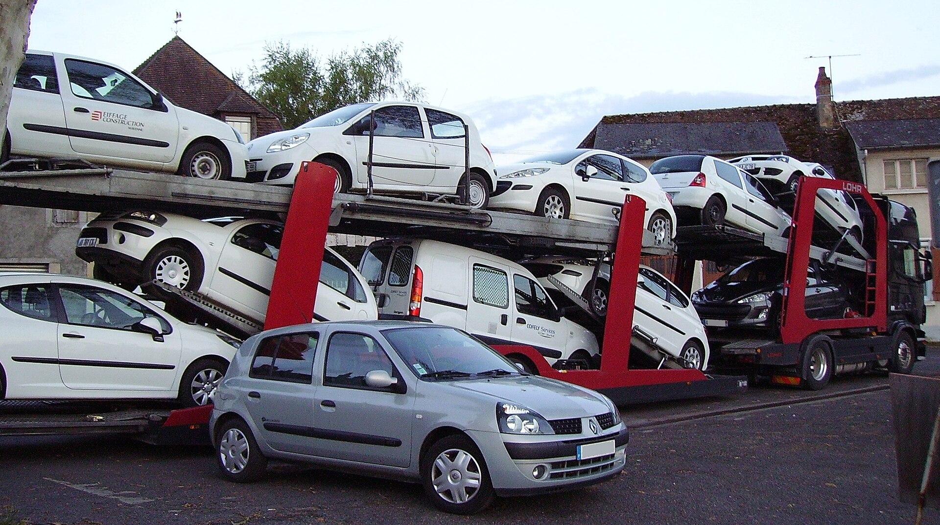 Cegonha aberta Scania com sistema Lohr, dois pisos carregados com carros e vans, num pátio de vila francesa
